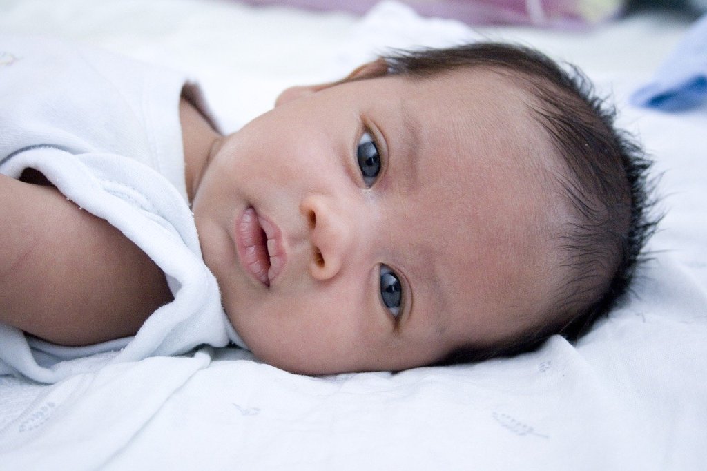 An infant lying down staring cutely at the camera. 